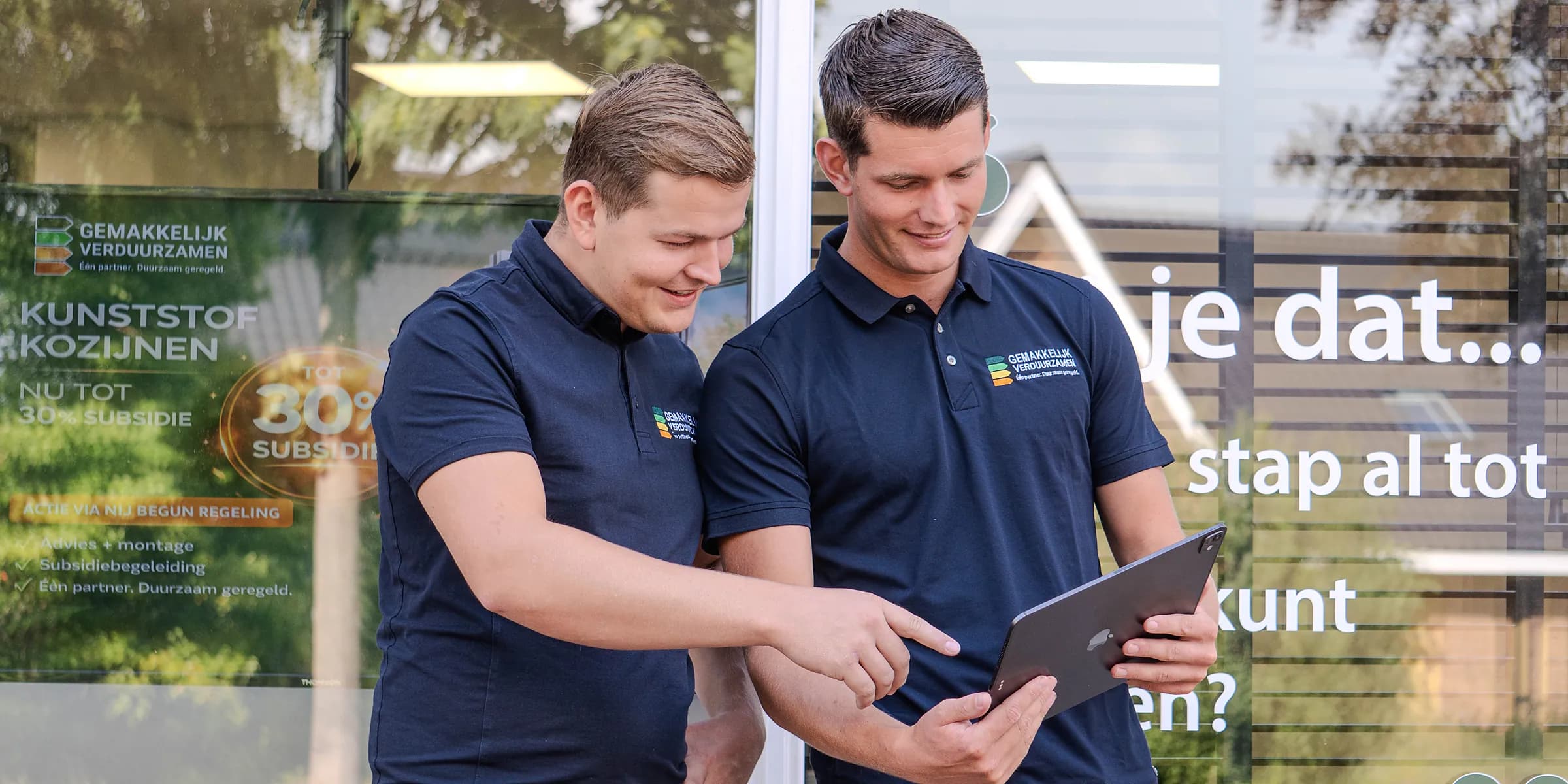 De twee adviseurs bekijken samen een woning op een tablet, voor het kantoor in Marum.
