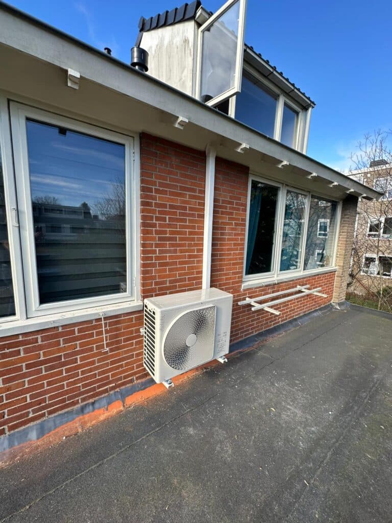 Buitenunit van een hybride warmtepomp tegen de gevel.