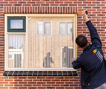 Een monteur meet een kozijn op met een rolmaat, buiten bij de woning.
