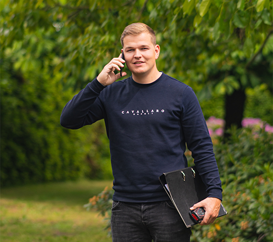 Jonge man in een tuin belt terwijl hij een map en meetlint vasthoudt.