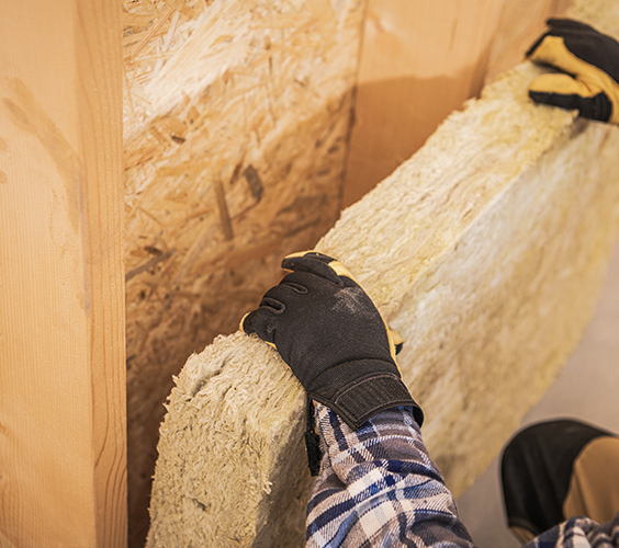 Isolatiemat wordt met handschoenen in houten wandvulling gedrukt om spouwruimte te isoleren.